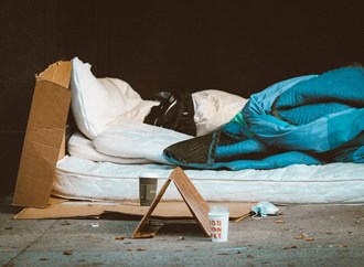 Mattress with sleeping bad on roadside with homeless sign and cup for donations